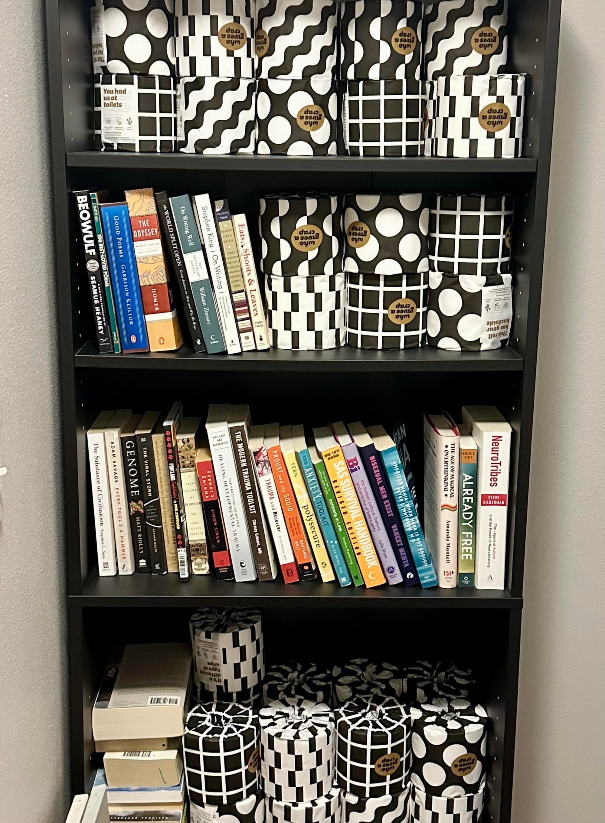 A black IKEA bookshelf on which three of the four shelves are more filled with stacks of toilet paper rolls than they are with books.